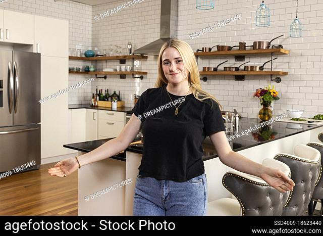 Portrait of a young woman standing in her kitchen with her arms outstretched in with a welcoming expression, looking at camera