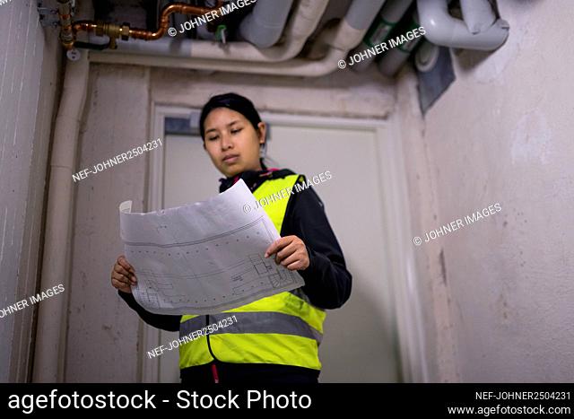 Female plumber holding blueprint and checking pipes