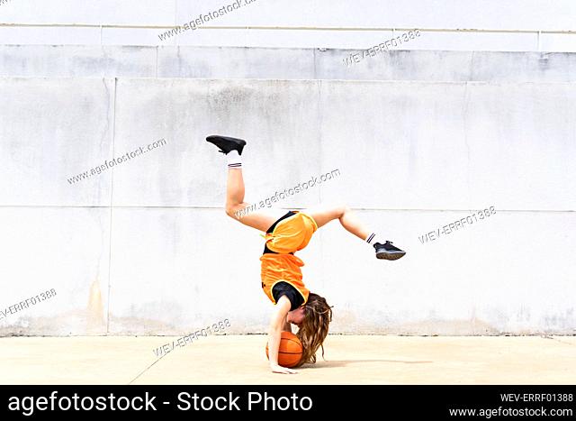 Teenage girl doing acrobatics with basketball outdoors