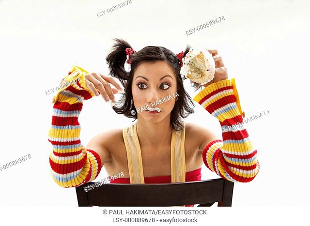 Beautiful Latina girl eating a cupcake with her fingers looking cross eyed, isolated