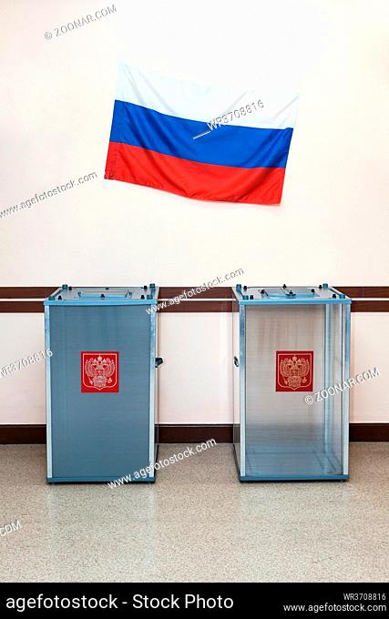 Two ballot boxes for voting in the elections with coat of arms Russia and the national flag of the Russian Federation hanging on the wall in the polling station