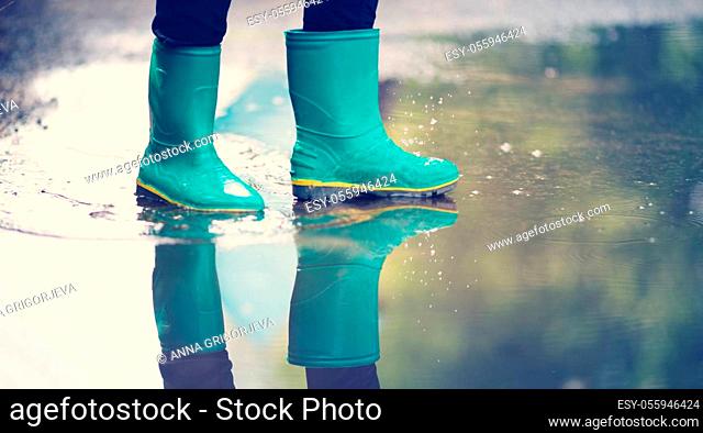 Child walking in wellies in puddle on rainy weather. Boy under rain in summer