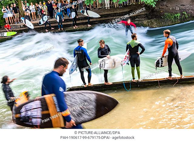 17 June 2019, Bavaria, Munich: A dozen surfers are waiting at the edge of the Eisbach wave for their turn. The spot in the English Garden is one of the tourist...