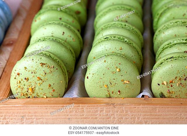 Fresh baked pistachio green macaroon pastry cookies (macarons, macaroni) in wooden box of retail store display, close up, high angle view