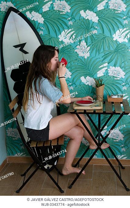 Young woman drinking coffee, in a cafe, next to your surfboard