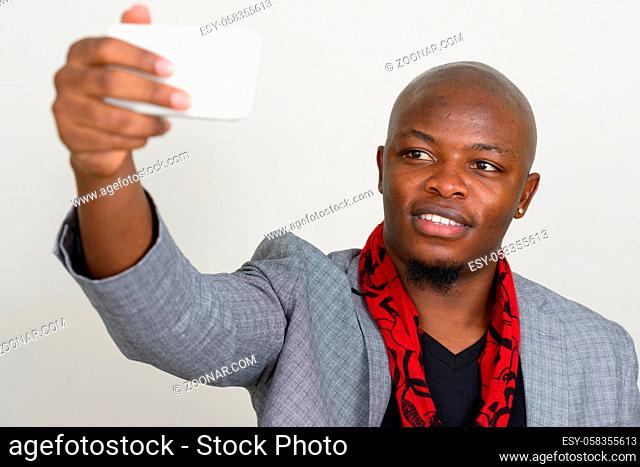 Studio shot of young handsome bald African businessman in suit wearing scarf against white background