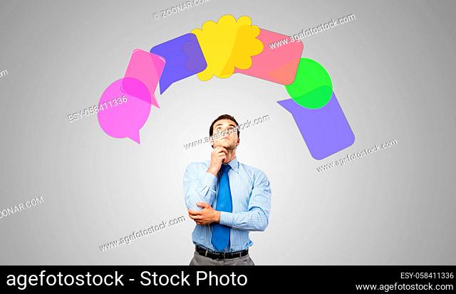Young thoughtful businessman and colorful speech bubbles above head