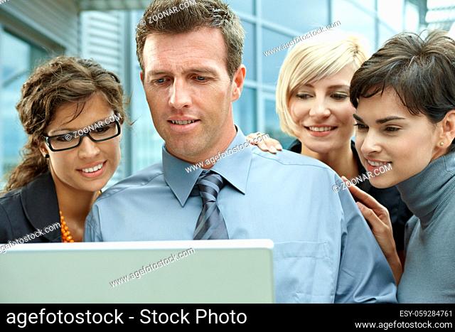 Team of business people looking at laptop computer outdoor in front of office building