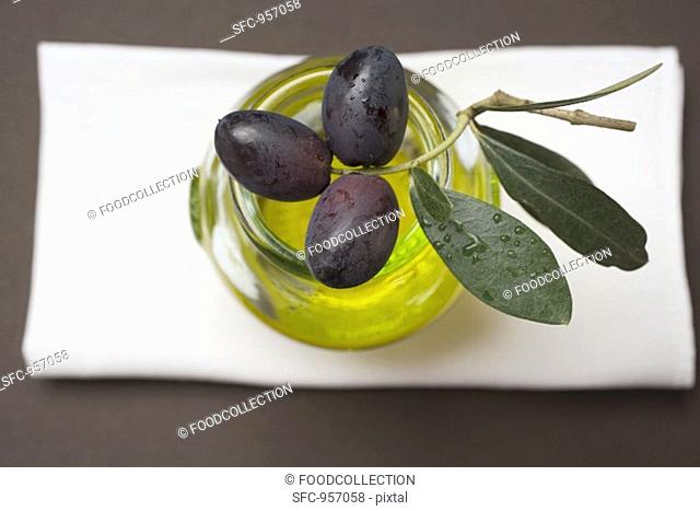 Black olives on twig on glass of olive oil