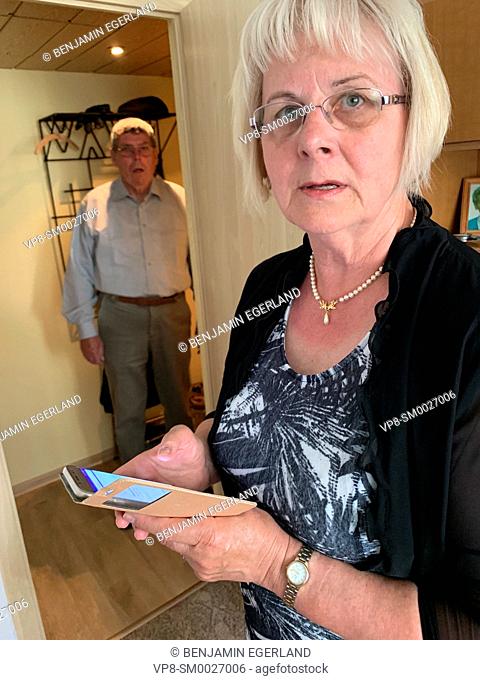 confused senior woman holding smartphone at home next to baffled senior husband, in Cottbus, Germany