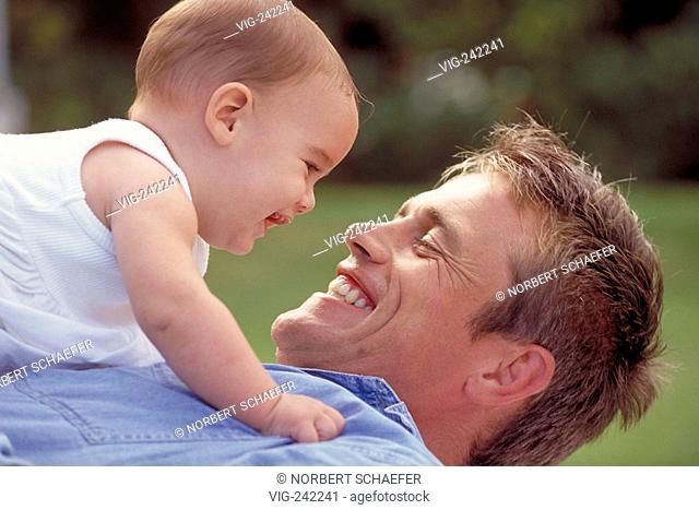 outdoor, portrait, father wearing jeans shirt lies with his baby on his body on a meadow  - GERMANY, 29/09/2004