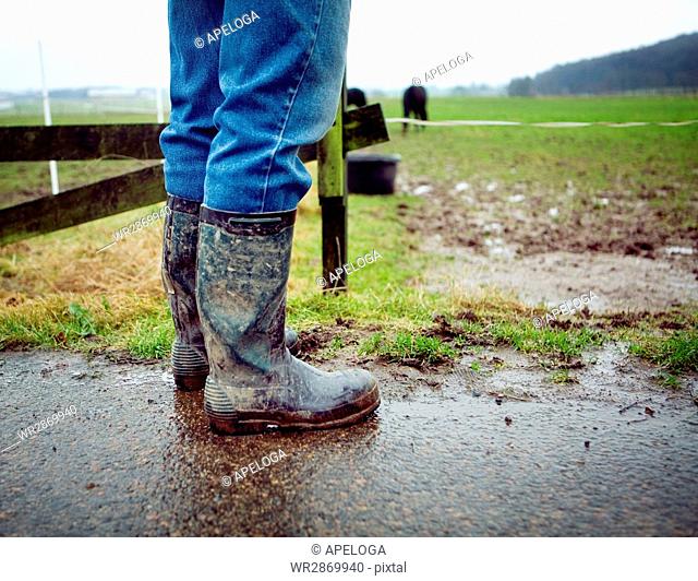 Low section of person in messy boots standing on field