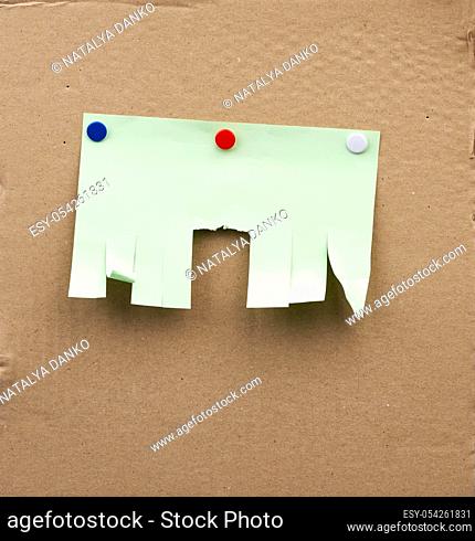 blank paper green ad with torn edges attached with iron buttons on a brown cardboard surface, backdrop for sales and messages