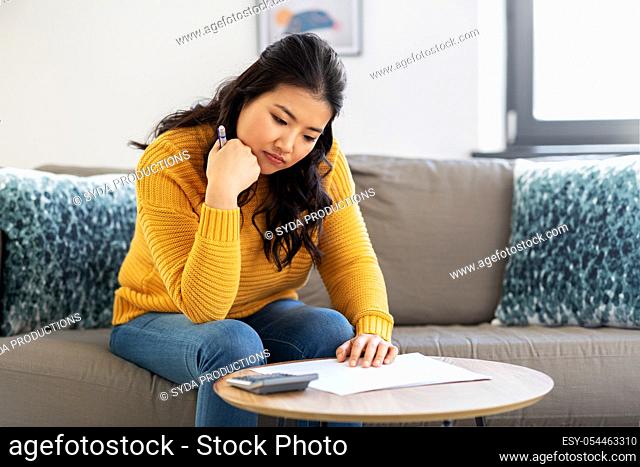 sad asian woman with papers and calculator at home