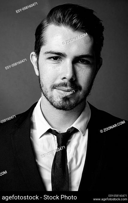 Studio shot of young handsome bearded businessman against gray background in black and white