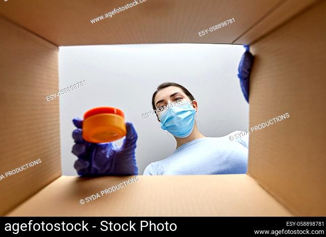woman in mask unpacking parcel box with cosmetics