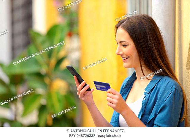 Happy woman paying online using credit card and smart phone in the street