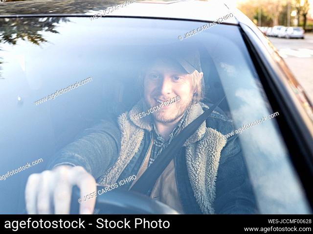 Smiling mid adult man driving car seen through windshield