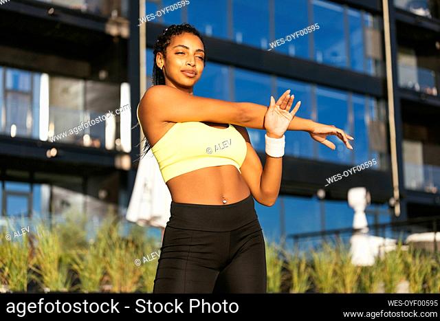 Smiling young woman stretching arms during sunny day