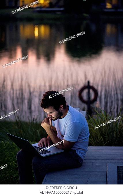 Man using laptop computer on lakeshore deck