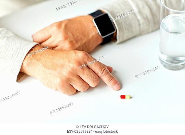 age, medicine, health care and people concept - close up of senior man with glass of water and pill looking at wristwatch