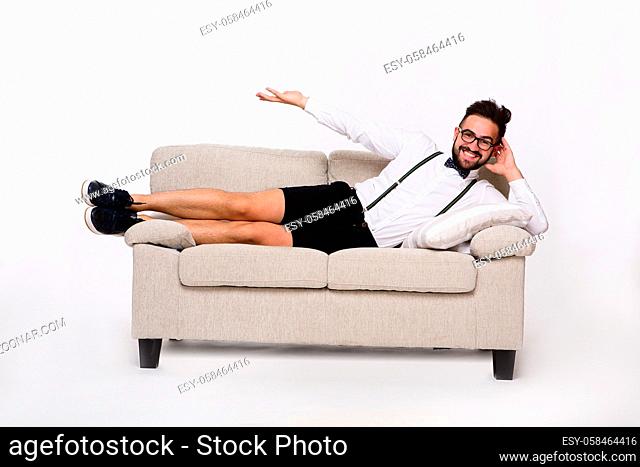 Picture of happy smiling handsome man lying on couch or sofa. Cheerful man in shirt and shorts demonstrating or representing something with his hand
