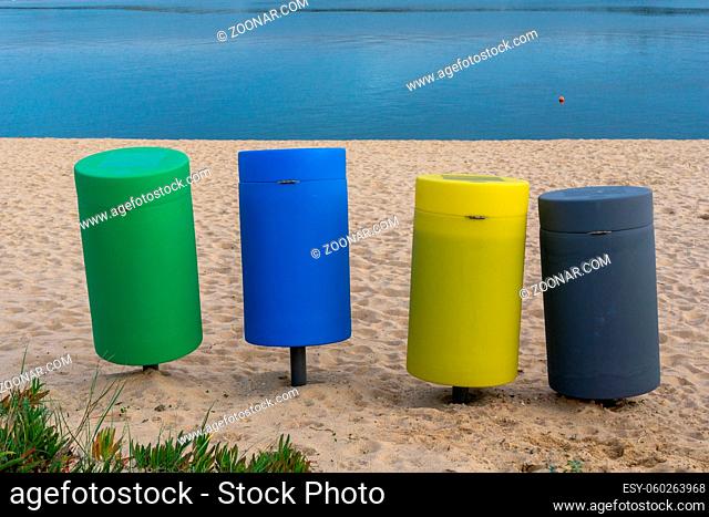 Four colorful recycling bins on a sandy beach