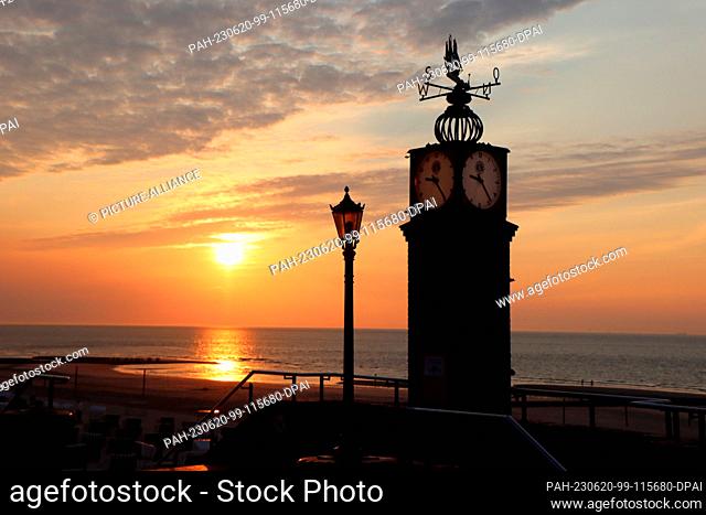 PRODUCTION - 18 June 2023, Lower Saxony, Wangerooge: The sun sets behind the so-called pudding clock on the beach promenade of the island of Wangerooge