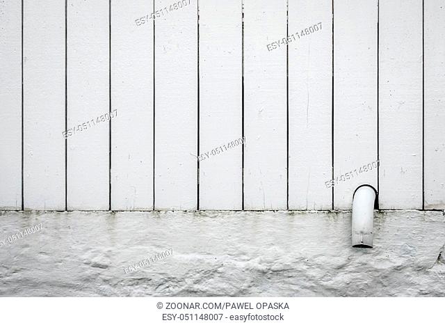 Detail of a small pipe tip sticking out of a white wooden fence