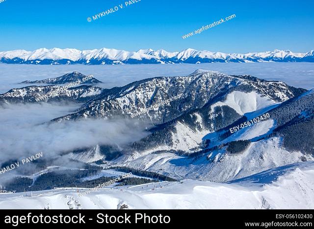 The tops of winter mountains and mist in the valleys in a ski resort. Sunny weather and blue sky. Aerial view