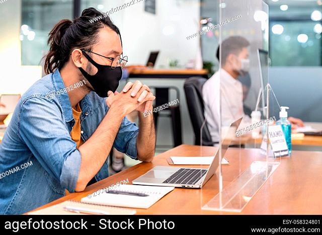 Asian office employee businessman wear protective face mask work in new normal office with interracial colleague in background as social distance practice...