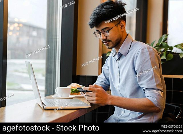 Freelancer using smart phone at table in cafe