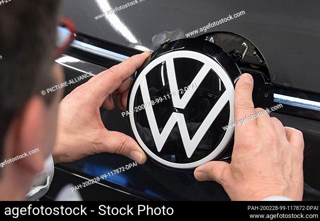25 February 2020, Saxony, Zwickau: An employee of Volkswagen Sachsen in Zwickau places the VW logo in the front of the VW ID.3
