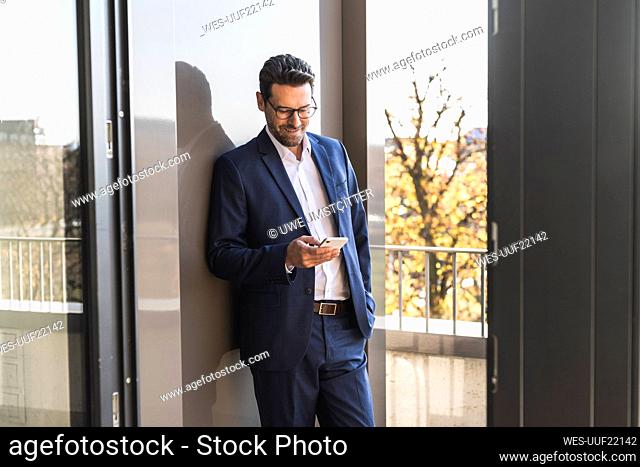 Male entrepreneur using mobile phone while standing with hand in pocket by balcony at office