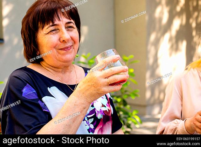 Portrait of attractive smiling middle-aged woman with straight dark hair, holding glass of lemonade. Senior woman outdoors at the cafe