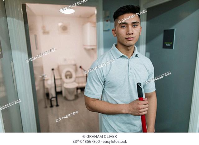 Portrait of a young, male cleaner at work. He is holding a mop
