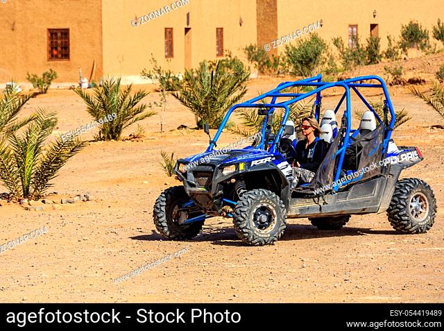 Itrane, Morocco - Feb 24, 2016: blue Polaris RZR 800 with woman pilot in a small Berber village in Morocco desert near Merzouga