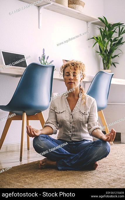Woman sitting on the floor at home with casual clothes doing meditation in lotus yoga position. Mindfulness exercise on the carpet in apartment