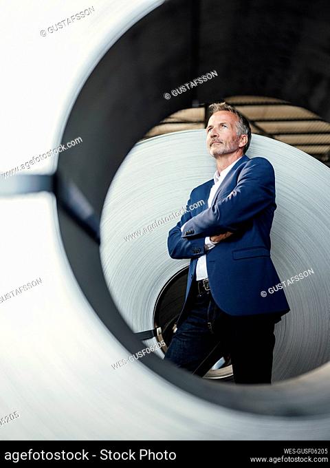 Thoughtful businessman with arms crossed standing in steel mill