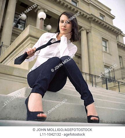 Woman sitting on steps of Public Building pulling on her necktie