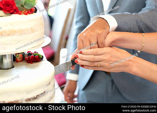 PRODUCTION - 21 August 2021, Baden-Wuerttemberg, Elzach: A bride and groom cut the wedding cake during the wedding reception. Photo: Silas Stein/dpa