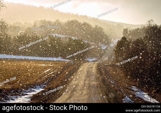Light shines through snowy weather on a curved country road, backlit snow particles making image soft