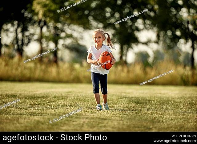 Smiling girl with rugby ball walking at sports field