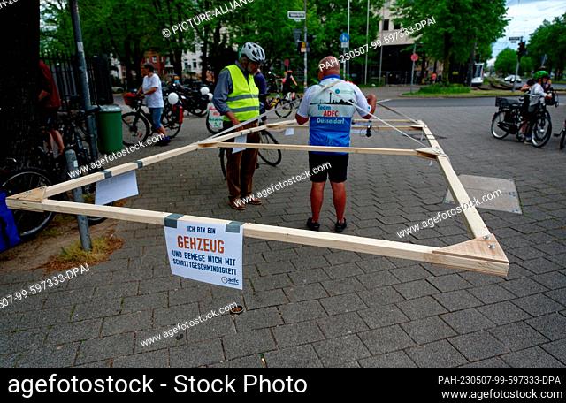 07 May 2023, North Rhine-Westphalia, Duesseldorf: A participant in a bicycle demonstration by the ADFC uses a wooden frame to demonstrate the space required by...