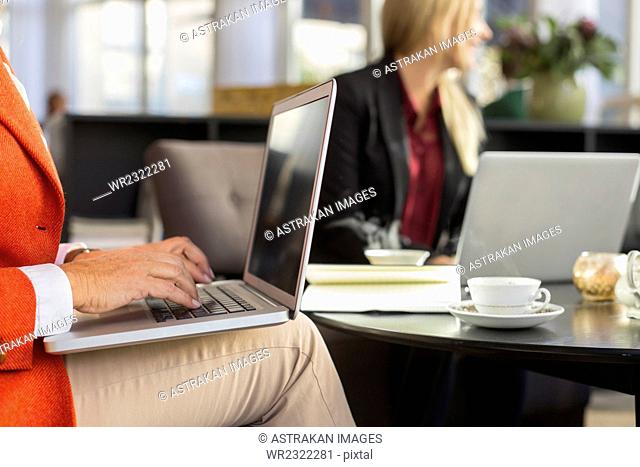 Midsection of businesswoman using laptop in meeting at restaurant