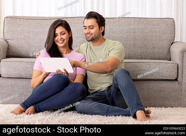 A young man and woman sitting in their room working on tablet phone
