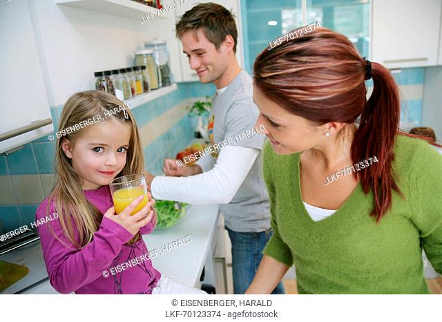 Family in kitchen, daughter drinking a glass of juice, Munich, Germany
