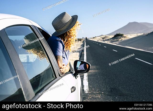 Woman outside window car parked on a long asphalt road side during travel trip. Summer road trip concept with female traveler looking desert and mountains out...