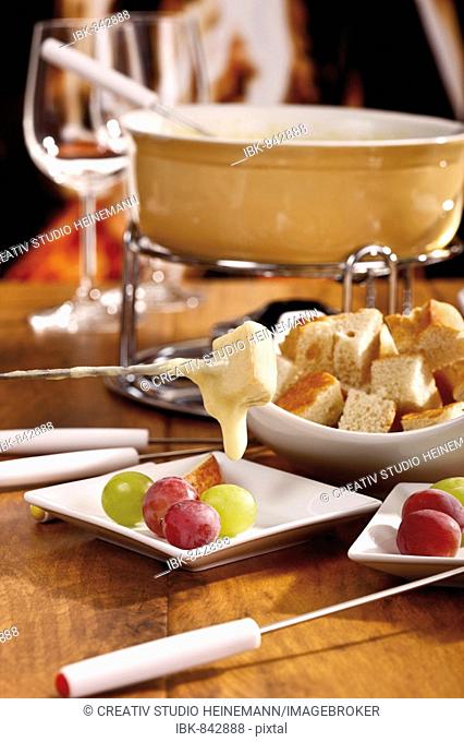A cheese-dipped bread cube on a fondue fork in front of a fondue pan