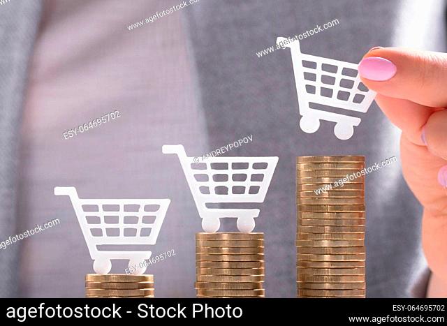 Businesswoman's Hand Placing White Shopping Cart On Top Of Golden Stacked Coins